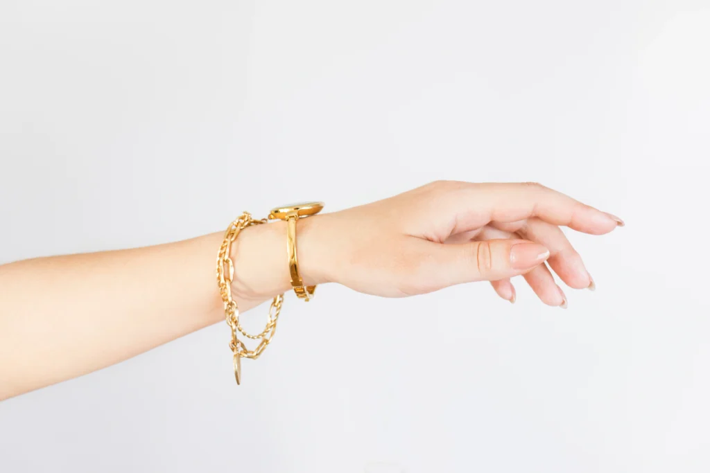 A hand adorned with a gold bracelet, a watch, and a delicate tennis bracelet is extended against a plain white background.